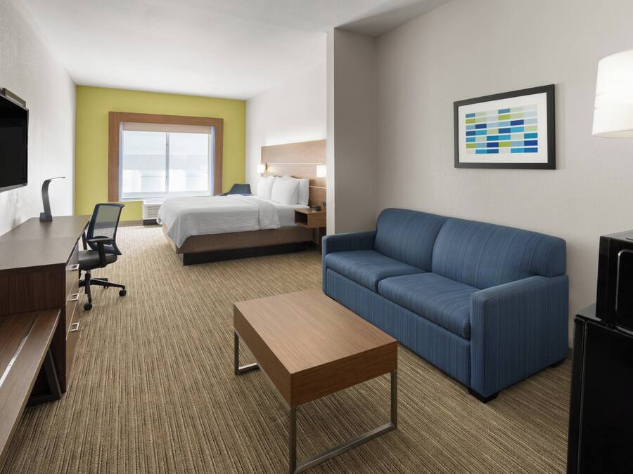 A hotel room with a bed, a blue sofa, a desk with a chair, a TV, and a framed picture on the wall.