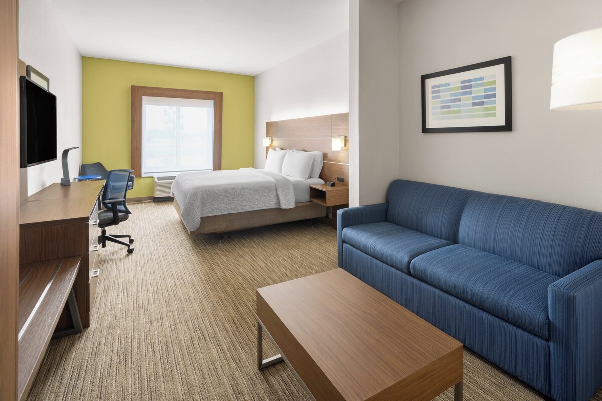 Quarto de hotel com cama, escrivaninha, poltrona, sofá e televisão.