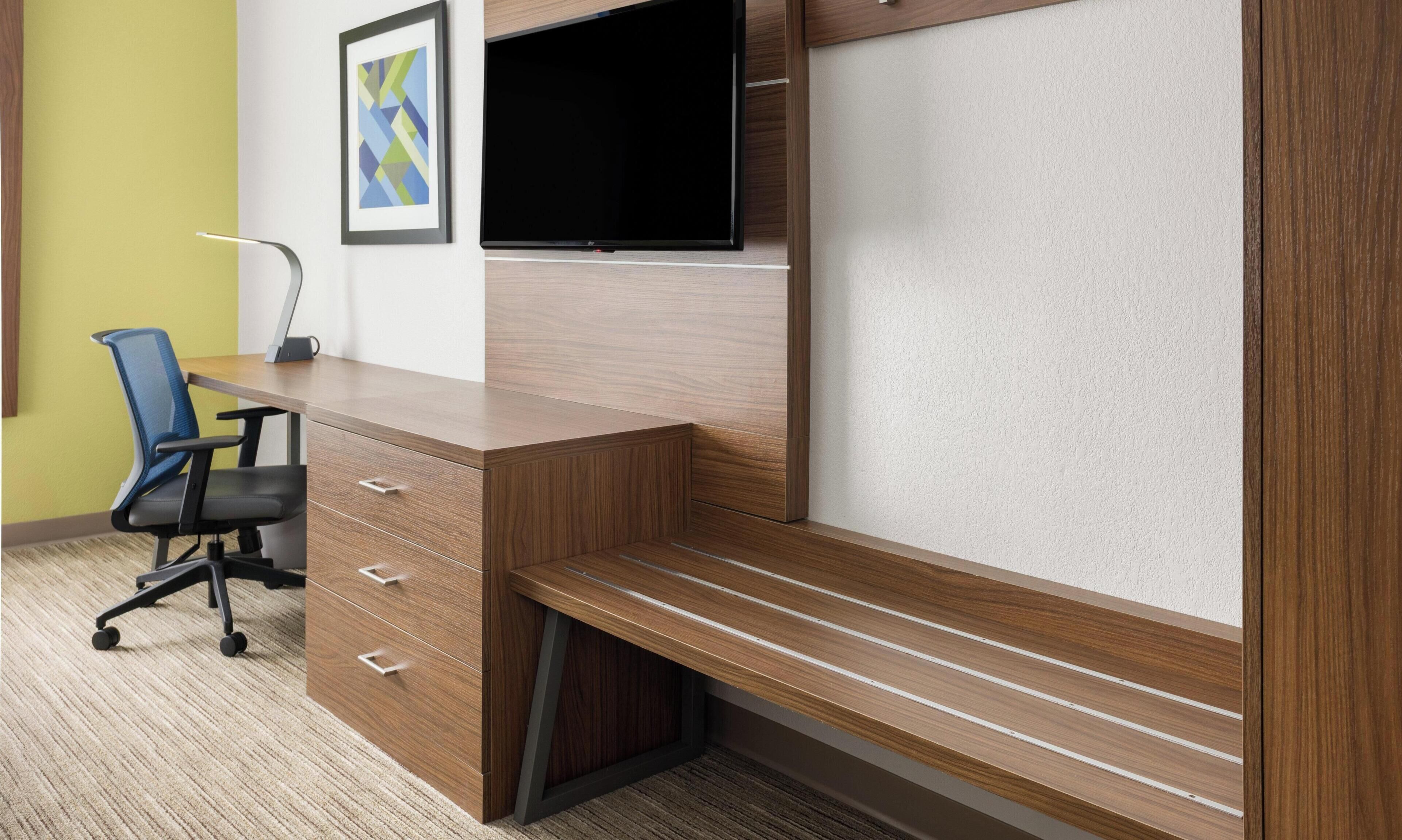 A modern office desk with a chair, a flat-screen TV, and a framed abstract artwork on the wall.