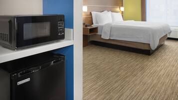 Habitación de hotel con microondas, un cesto de basura pequeño, cama con ropa blanca, mesita de noche con lámpara y ventana con vistas.