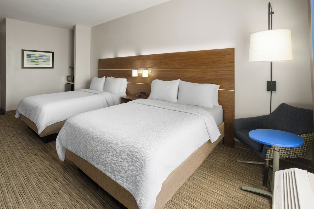 A hotel room with two beds, a desk, a chair, a lamp, and a framed picture on the wall.