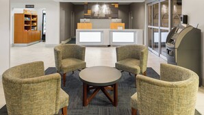A lobby with a reception desk, two armchairs, a round table, a vending machine, and a self-service kiosk. - Holiday Inn Express Hotel & Suites New Iberia - Avery Island by IHG (New Iberia)