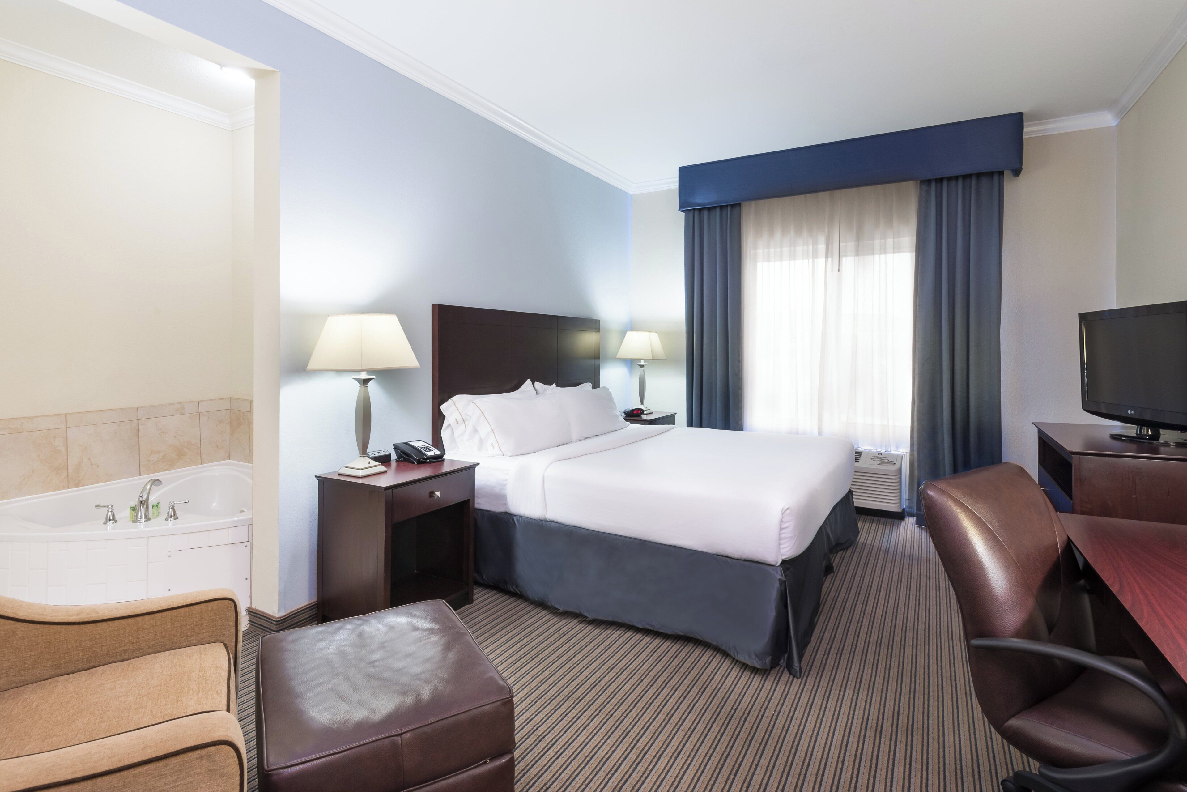A hotel room with a bed, a desk, a chair, a television, a lamp, a telephone, and a bathroom with a bathtub and sink.