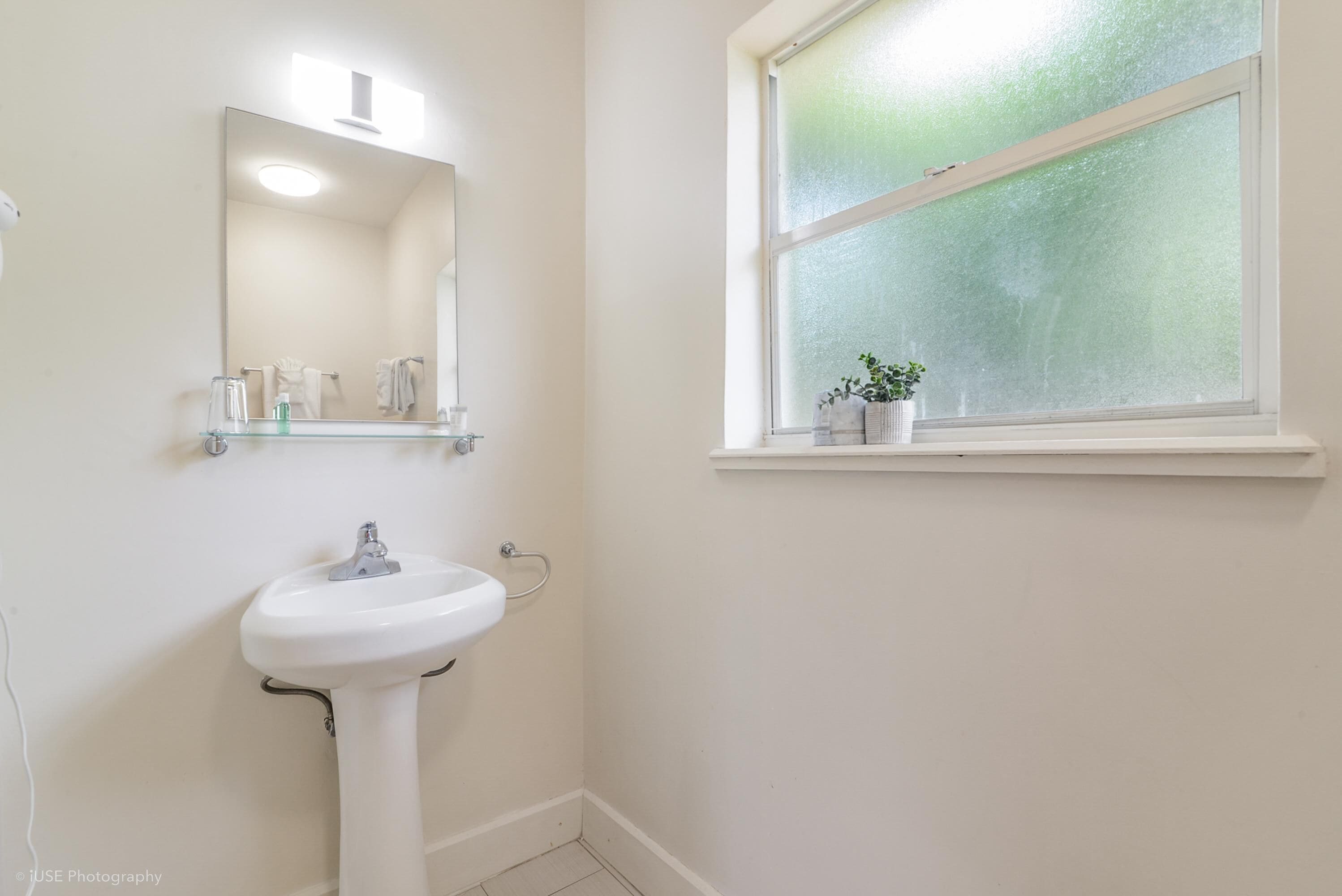 A bathroom with a white sink, a mirror, and a window with frosted glass.