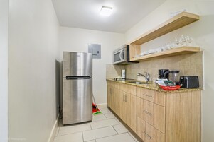A compact kitchen with a stainless steel refrigerator, a microwave, a sink, and wooden cabinets.