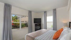 A bedroom with a bed, a TV, a dresser, and a window with curtains. - Soleado Hotel (Fort Lauderdale)