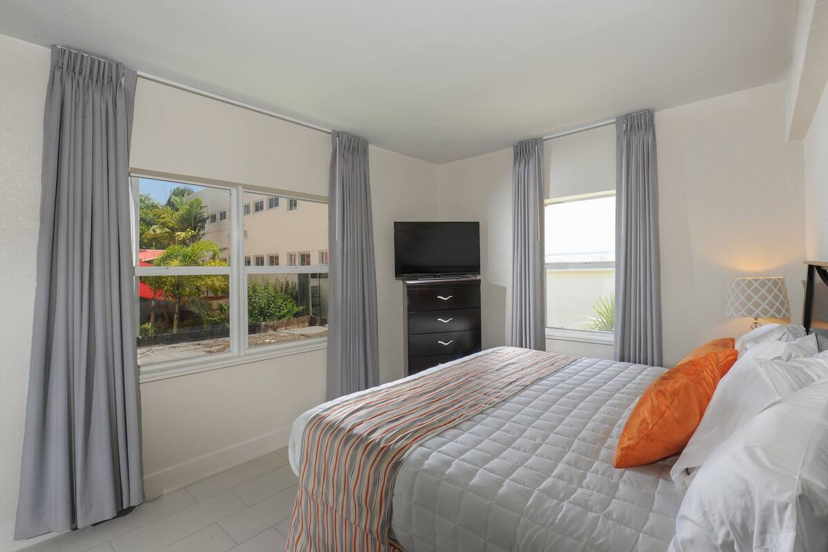 A bedroom with a bed, a TV, a dresser, and a window with curtains.