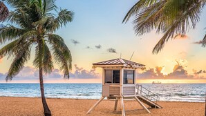 A lifeguard tower on a beach with palm trees and a sunset in the background. - Soleado Hotel (Fort Lauderdale)