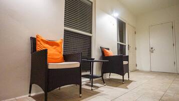 Un couloir avec deux fauteuils en osier, chacun agrémenté d’un coussin orange, et une petite table placée entre eux.