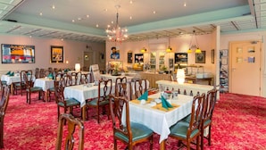 Un espace repas comprenant plusieurs tables et chaises, un lustre et un buffet.