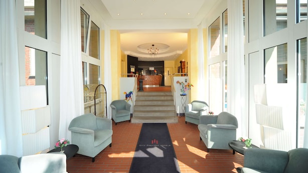 Un hall d’hôtel avec un escalier central, des canapés de couleur claire et un comptoir d’accueil.