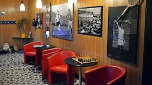 Une pièce aux murs en bois, avec des chaises rouges, une table d’échecs et des objets de collection sur le thème du sport.