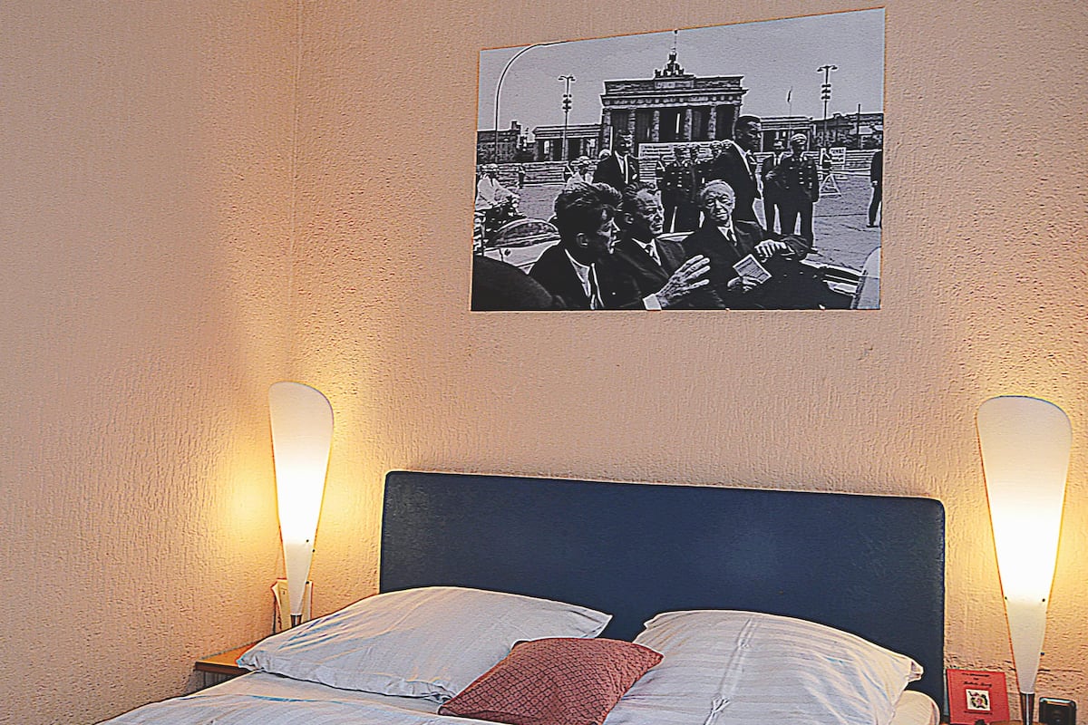 Uma cama com cabeceira azul, duas luminárias de apoio e um quadro na parede.