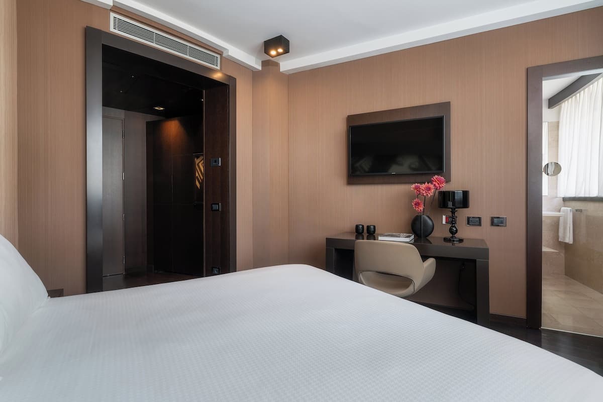 Habitación de hotel con una cama grande, un escritorio con silla, un televisor de pantalla plana y un baño visible a través de una puerta abierta.