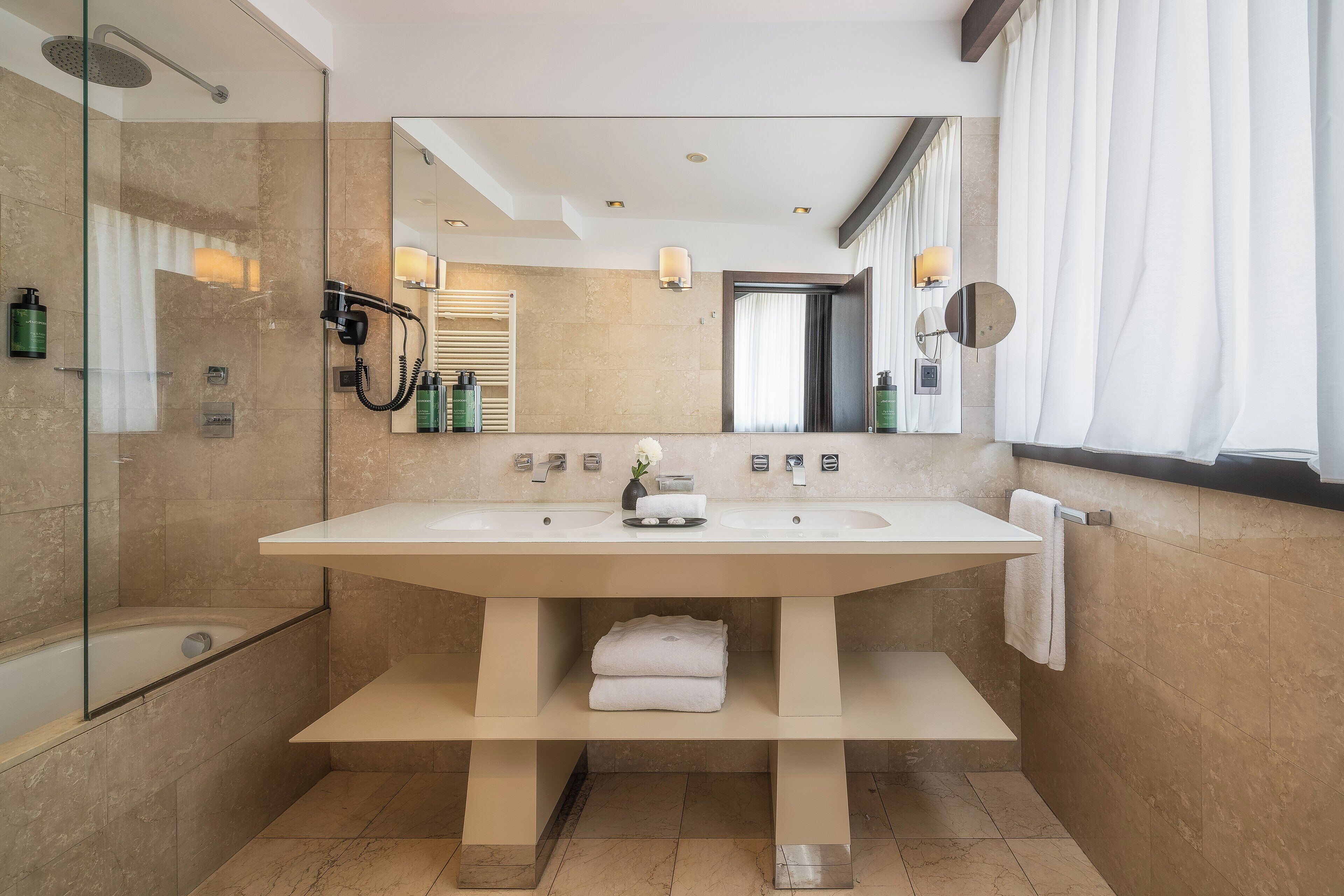 A modern bathroom with a large mirror, two sinks, a shower, and a towel rack.