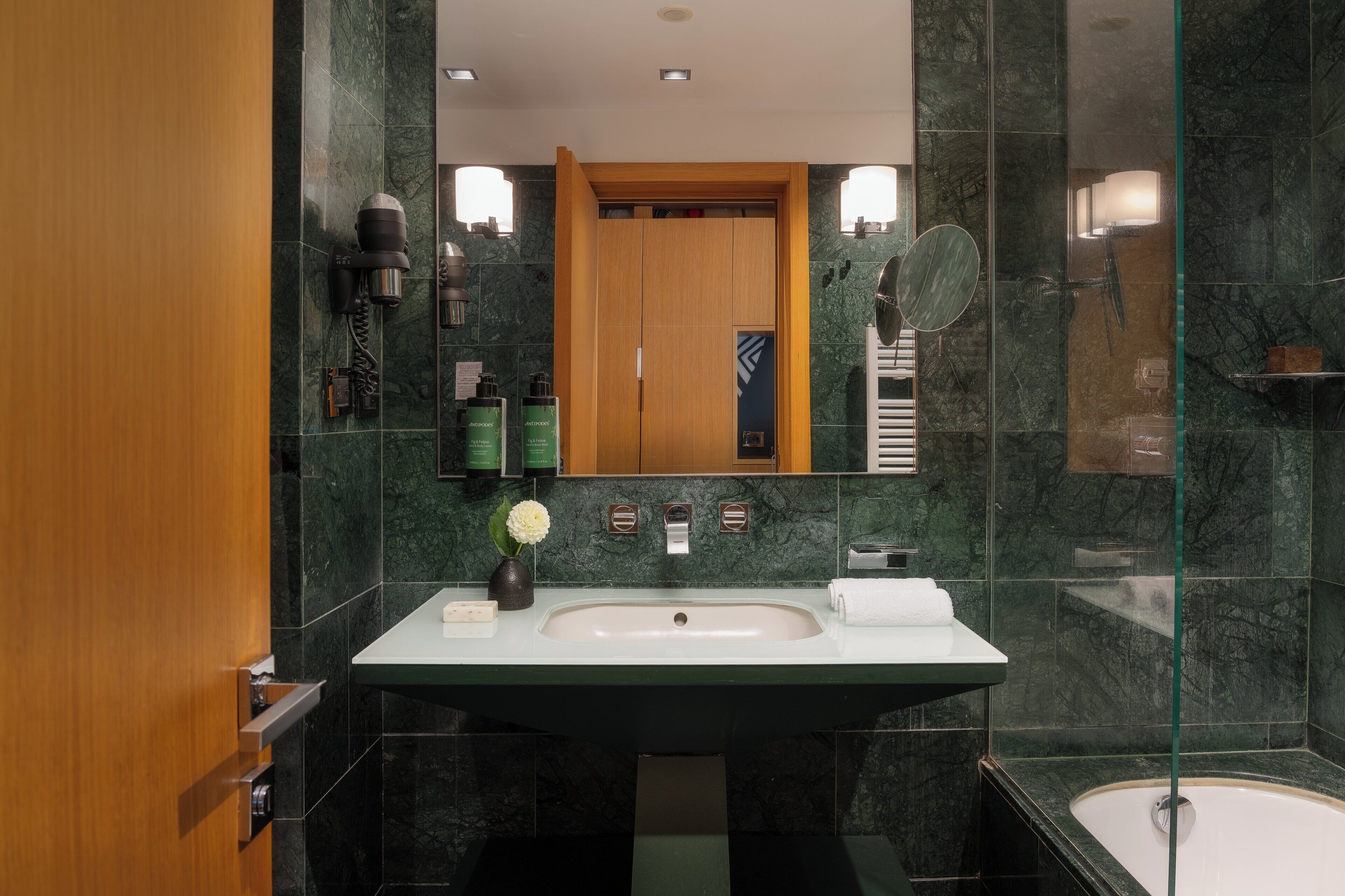 A modern bathroom with a large mirror, a sink, a shower, and a wooden door.
