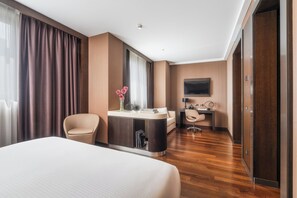 A hotel room with a large bed, a desk, a chair, a TV, and a bathroom. - Crowne Plaza Milan City by IHG (Milan)
