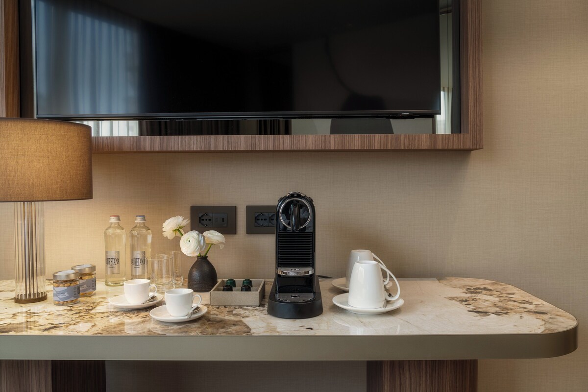 Une chambre d’hôtel dotée d’un comptoir en marbre, d  ’une machine à café, d’un vase rempli de fleurs et d’un téléviseur fixé au-dessus du comptoir.