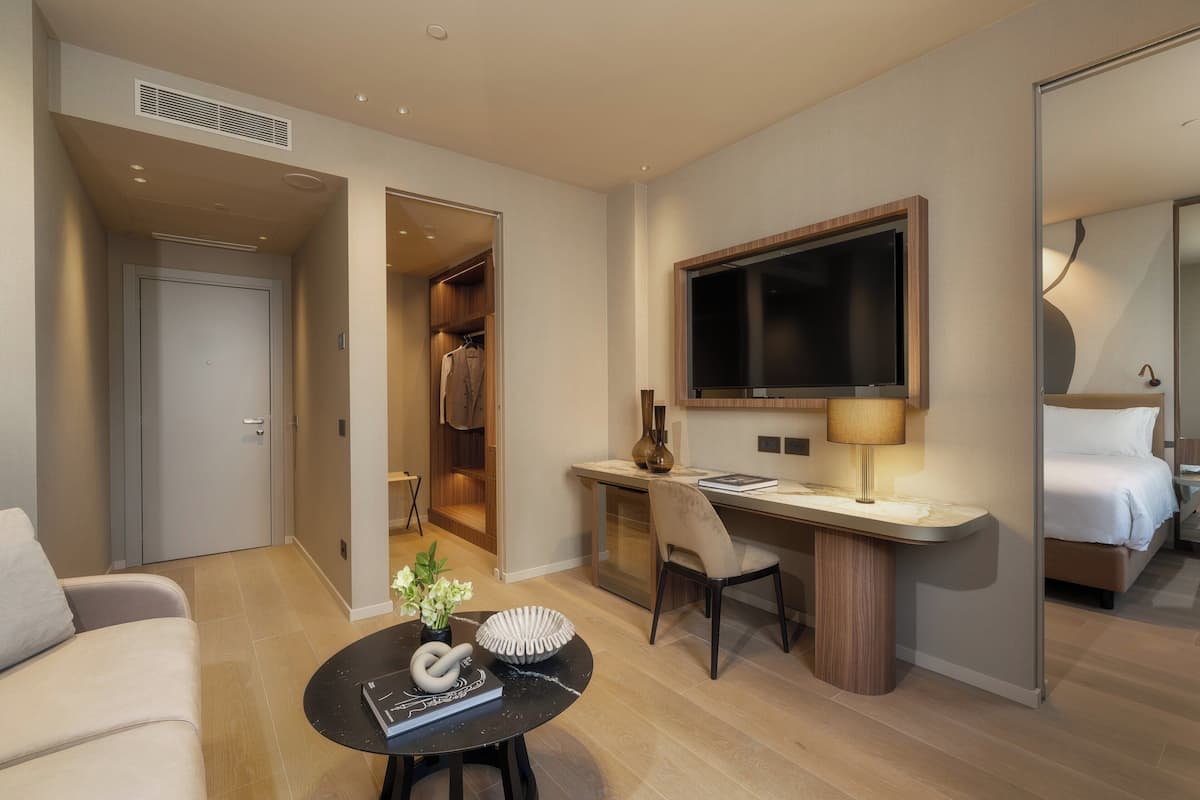 Una habitación de hotel moderna con una cama, un escritorio con silla, un televisor y una mesa de centro con adornos.