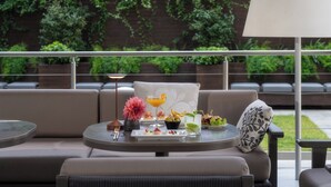 A modern outdoor seating area with a sofa, round tables, and a variety of food and drink items.
