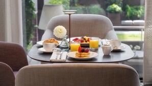 A breakfast table with a variety of food items, including pancakes, fruit, and beverages, set in a room with a view of greenery outside.
