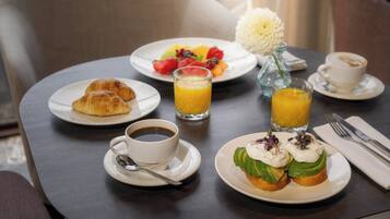 A breakfast setting with croissants, fruit, avocado toast, coffee, and orange juice on a table.