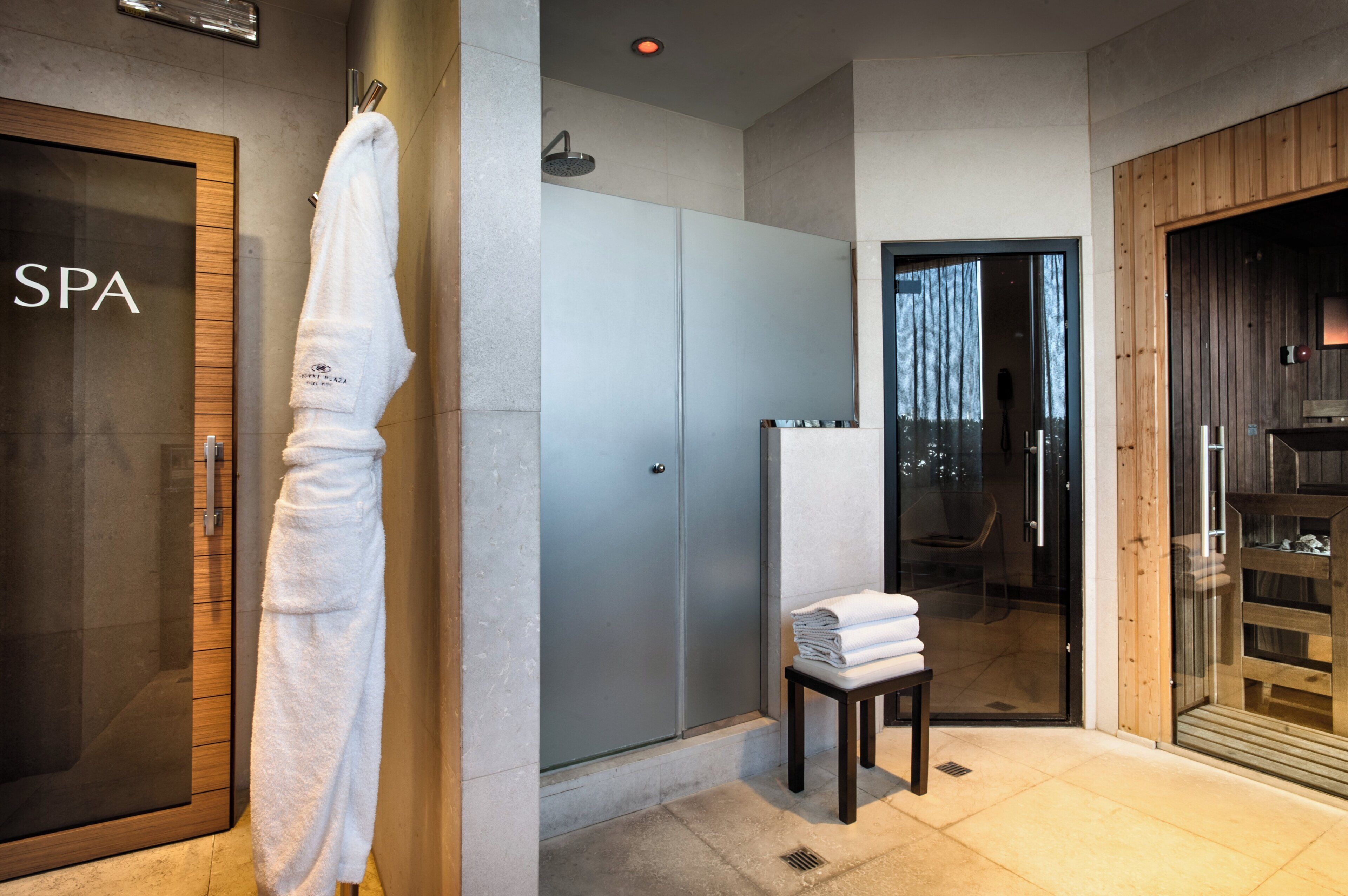 Un cuarto de spa con una puerta de madera que dice 'SPA', una toalla blanca colgada en la pared, un área de ducha y una pequeña mesa con toallas dobladas.