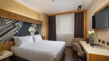 A hotel room with a large bed, a desk, a chair, a TV, and a window with curtains.