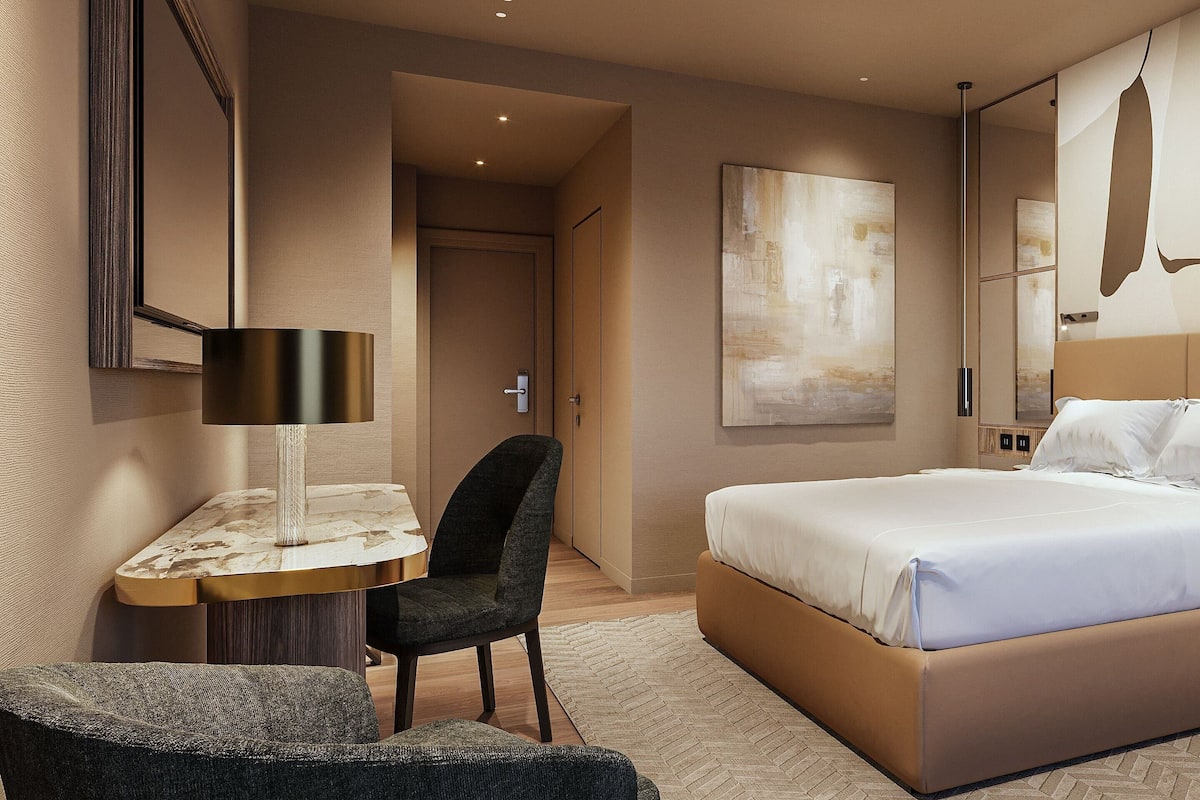 Una habitación de hotel moderna con una cama grande, un escritorio, una silla y un espejo.