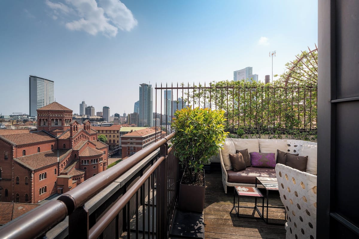 Una terraza en la azotea con zona de estar, una planta en maceta y vistas de la ciudad.