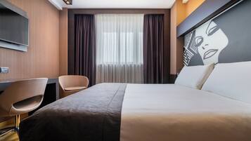 A hotel room with a bed, a desk, a chair, a TV, and a large window with curtains.