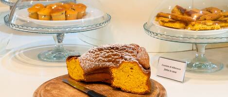 A display of various baked goods including a cake with a label, muffins, and pastries on glass stands.