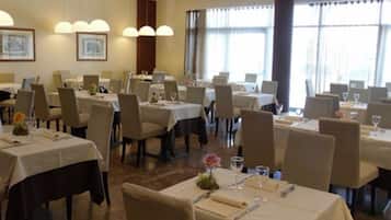 Un espace repas avec des tables dressées pour quatre personnes, chacune agrémentée d’une nappe blanche, de chaises et de couverts, notamment des verres à vin et des couverts de table.