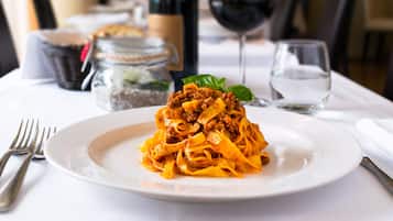 Een bord pasta met een vlees topping, een wijnglas en een waterglas op een tafel.