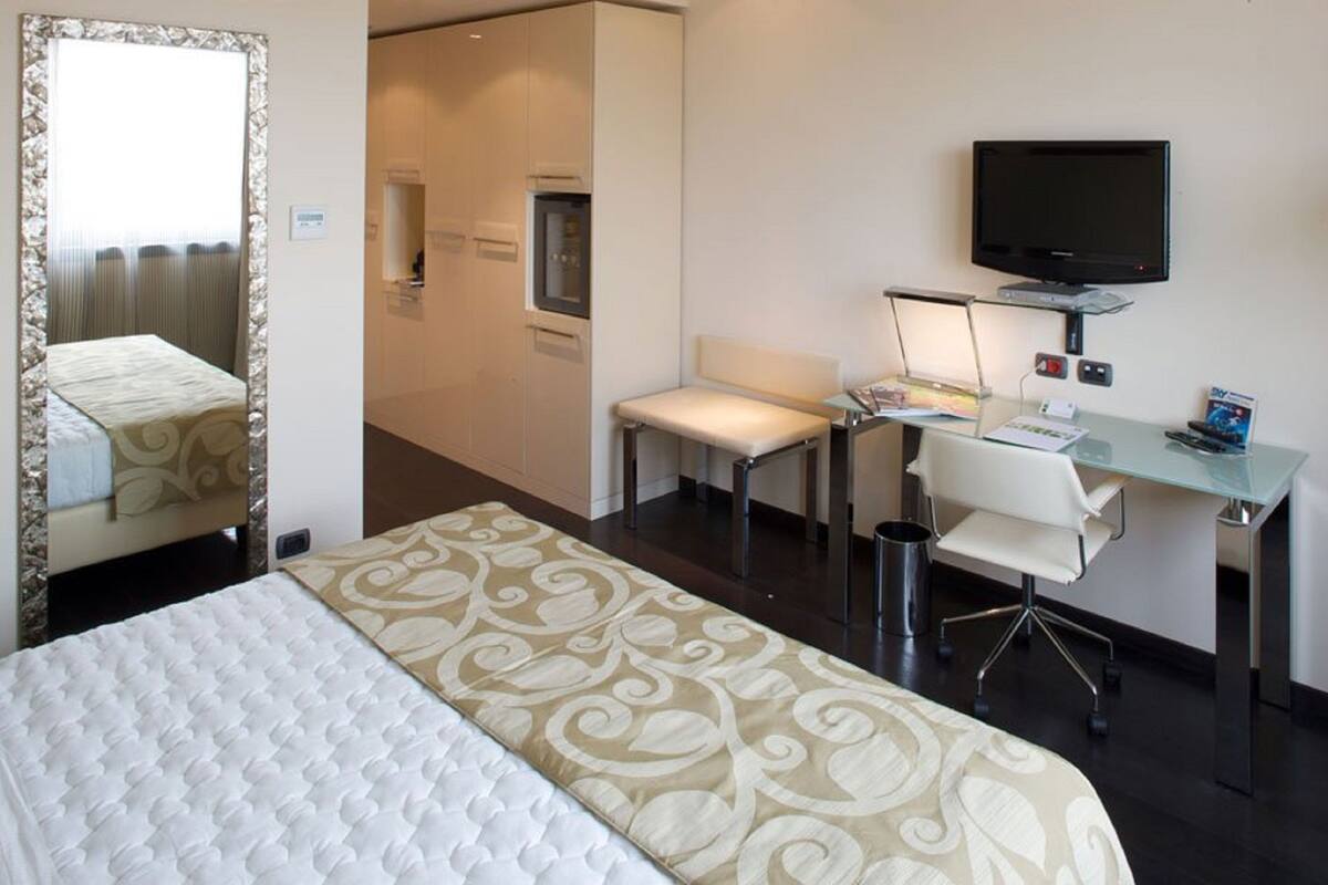 Una habitación de hotel con cama, escritorio, silla, televisor y una mesita.