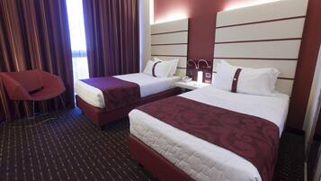 Habitación de hotel con dos camas, una silla roja y una mesita de noche con una lámpara.