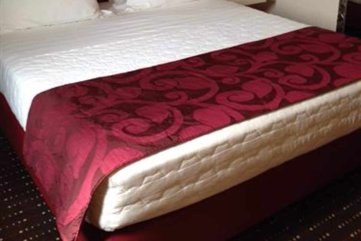 Una cama con colchón y almohadas blancas, y una colcha de cuadros rojos y negros.
