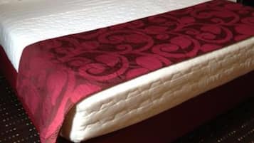Un lit avec un matelas et des oreillers blancs, une couvre-lit à motifs rouges et noirs, et une tête de lit blanche.