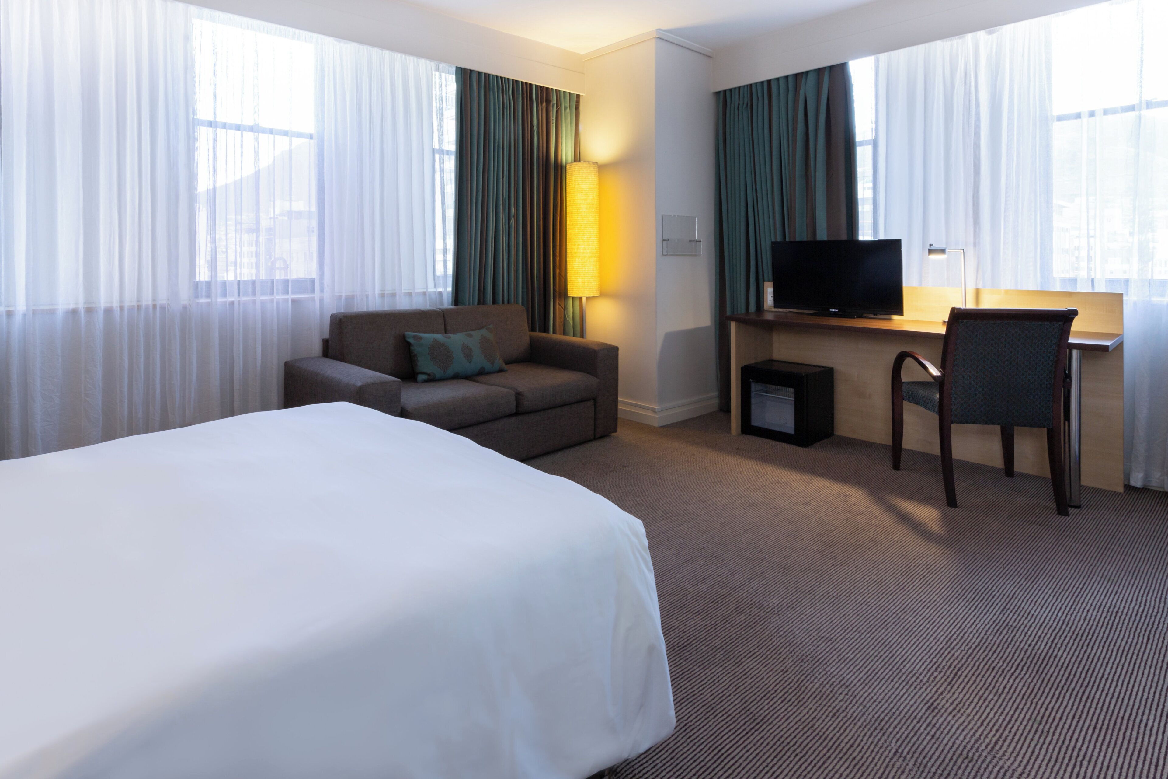 Una habitación de hotel con una cama grande, un escritorio con silla, un televisor y una lámpara.