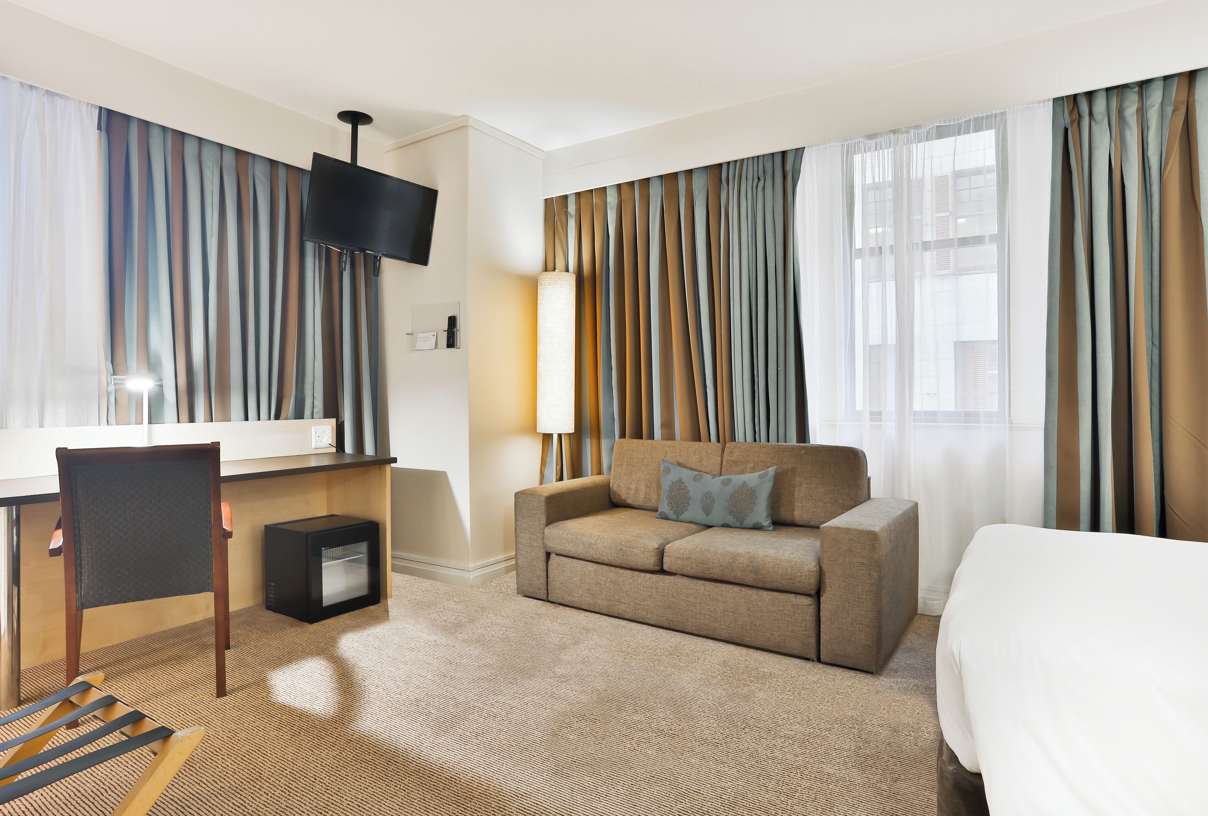 A hotel room with a sofa, a bed, a desk, a chair, a TV, and curtains.
