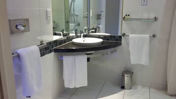 Un baño moderno con un lavamanos blanco, encimera negra y cabina de ducha de vidrio.