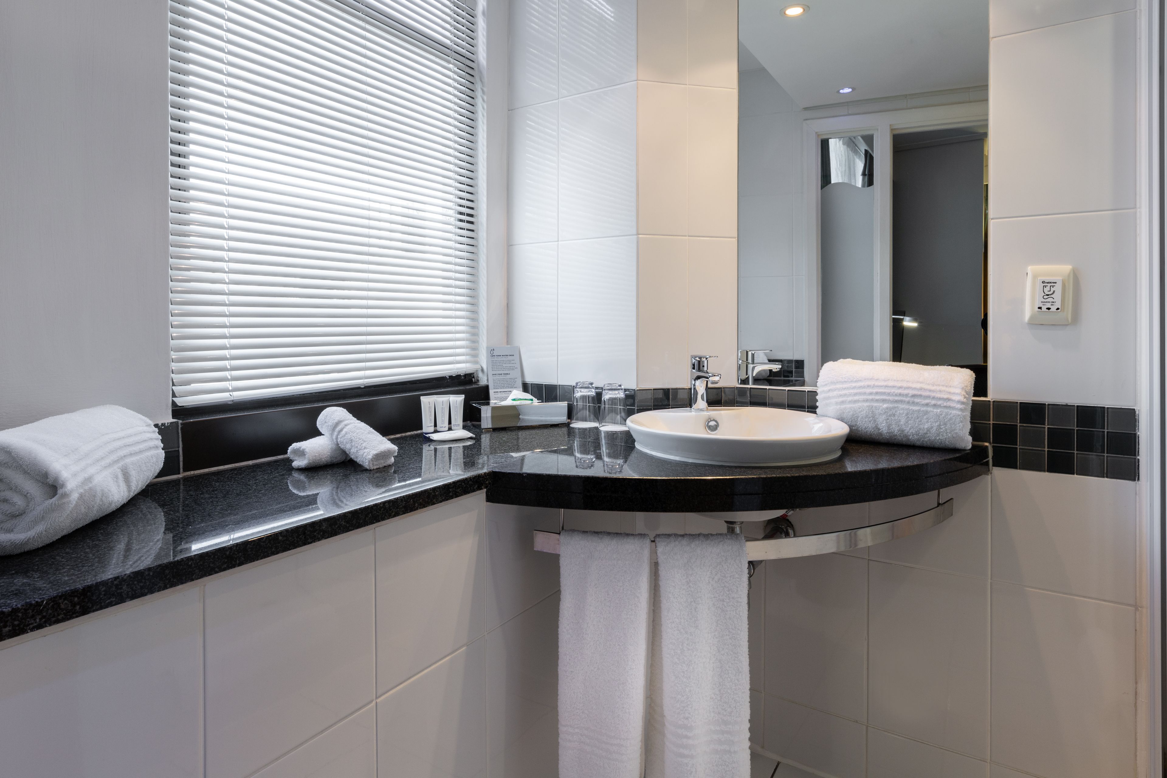 Un bagno moderno con un piano d'appoggio nero, lavandino bianco e uno specchio grande.