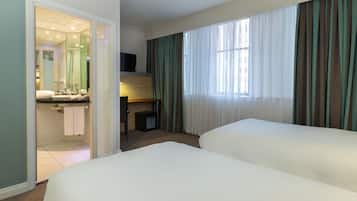 Habitación de hotel con dos camas, un escritorio, un televisor y un baño con espejo y lavamanos.