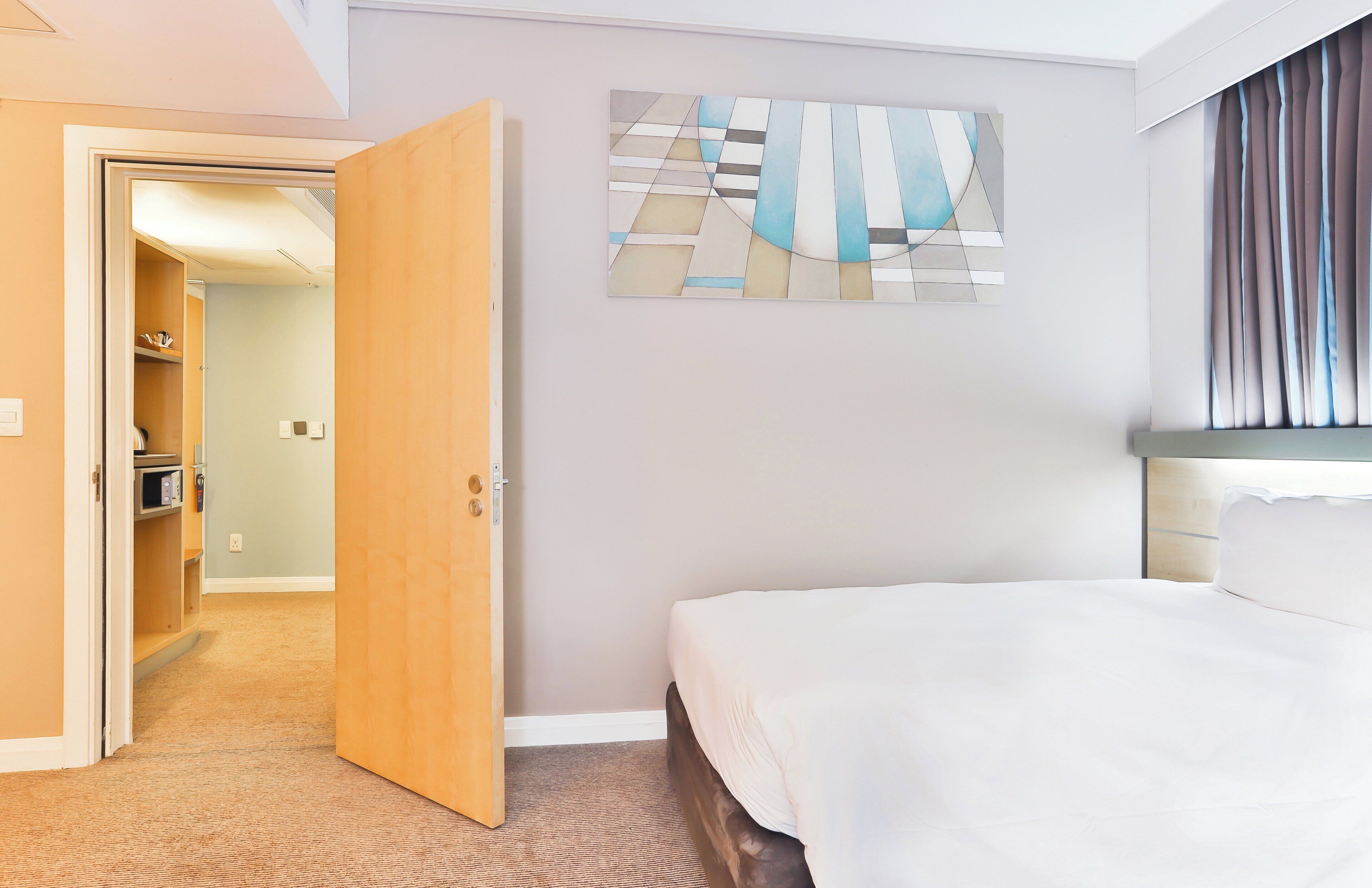 A hotel room with a bed, a painting on the wall, and an open door leading to a hallway.