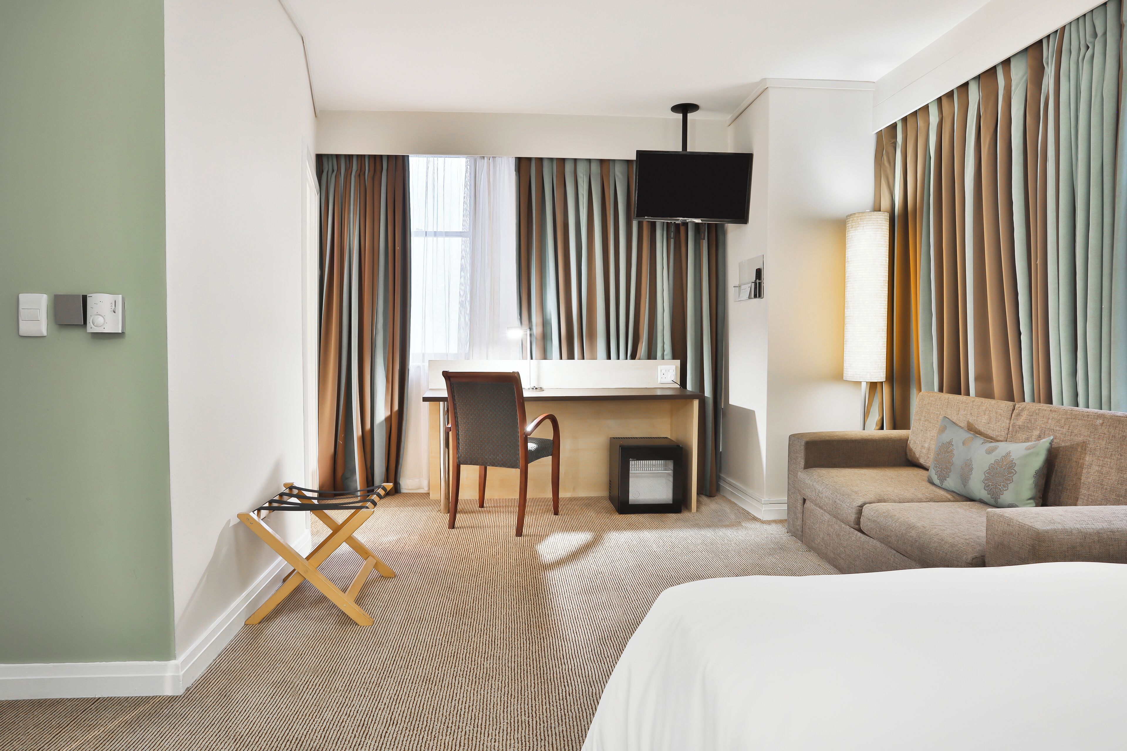 Une chambre d’hôtel avec un lit, un bureau, une chaise, une télévision et un canapé.