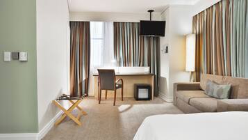 Une chambre d’hôtel avec un lit, un bureau, une chaise, une télévision et un canapé.