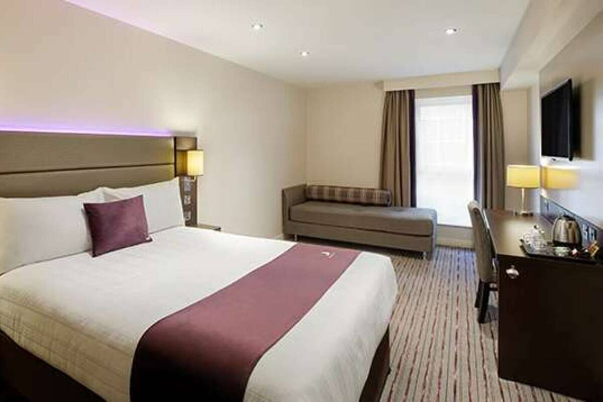 A hotel room with a large bed, a sofa, a desk, and a TV.