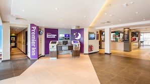 Egy szállodai előtér, amelyben recepció, bejelentkező pultok és egy „Premier Inn” feliratú tábla található.