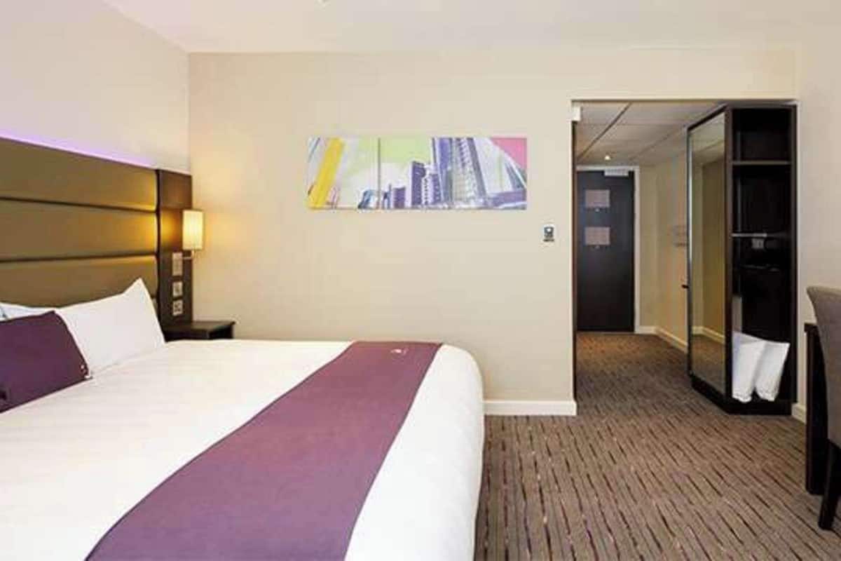 A hotel room with a large bed, a desk, a chair, a mirror, and a painting on the wall.