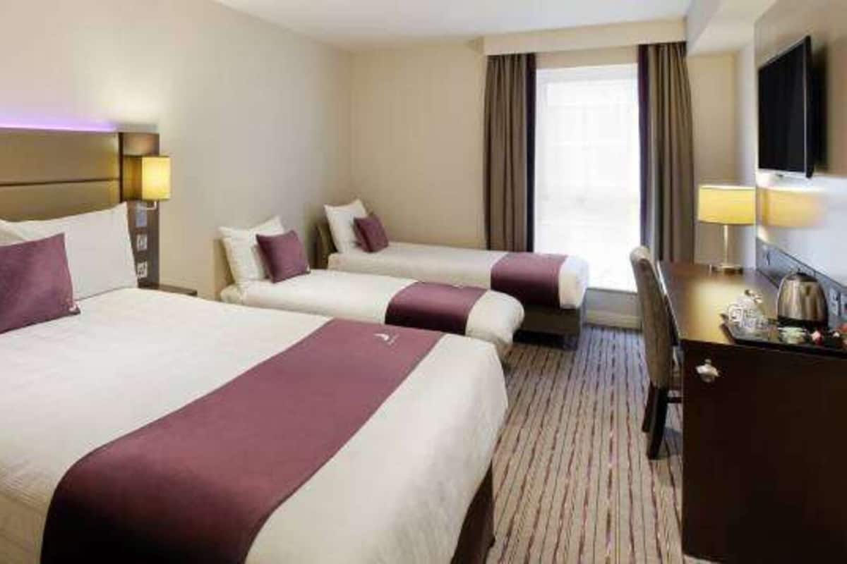 A hotel room with two beds, a desk, and a television.